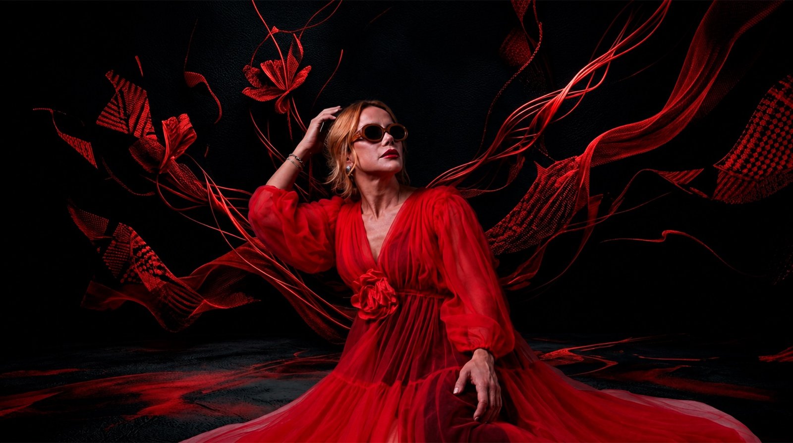 Carla Lemos de vestido vermelho e óculos escuros, em fundo preto com tecidos vermelhos