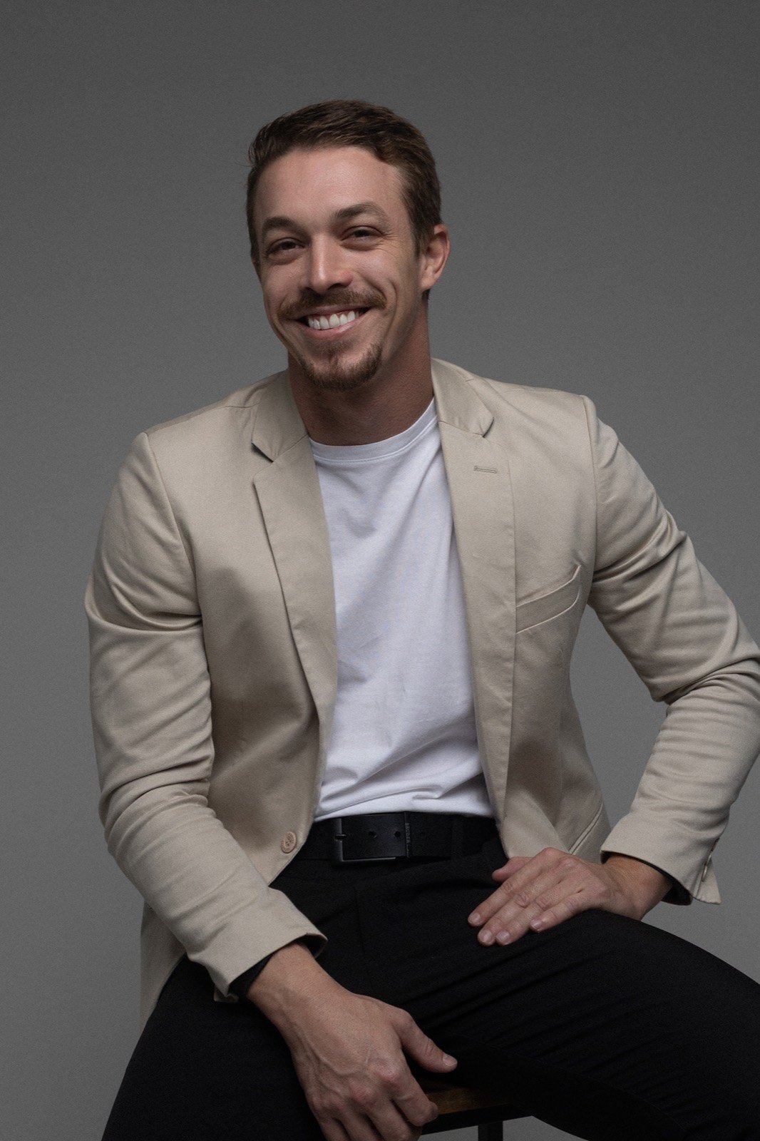 Felipe Fávaro de blazer bege, sorrindo, em ensaio de estúdio