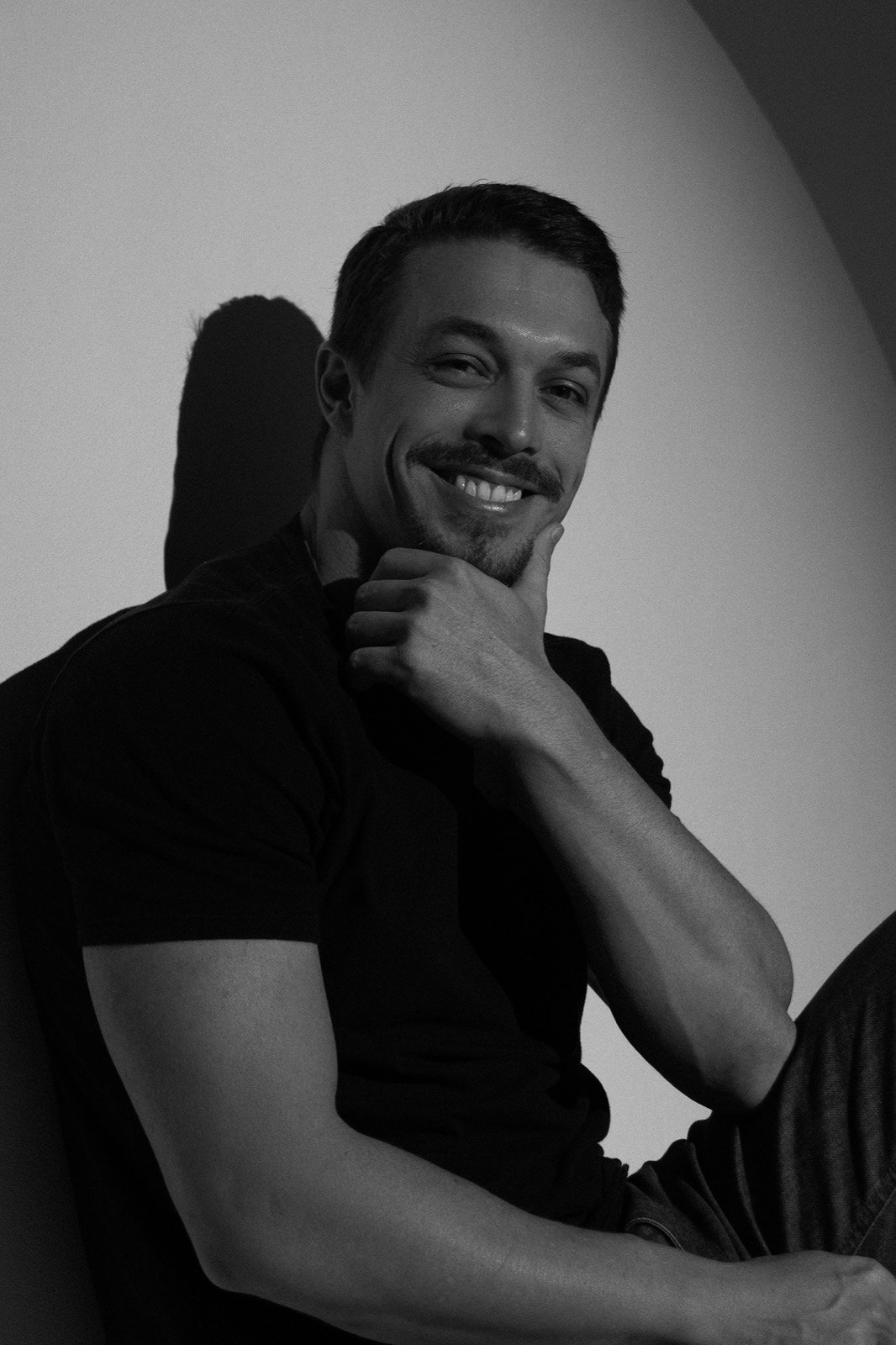 Felipe Fávaro sorrindo, sentado, com a mão no queixo